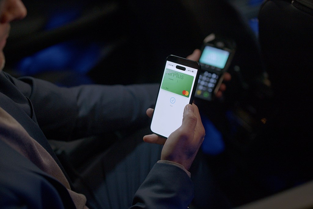 En hand håller en mobiltelefon med ett digitalt betalkort nära en betalterminal i en bil.