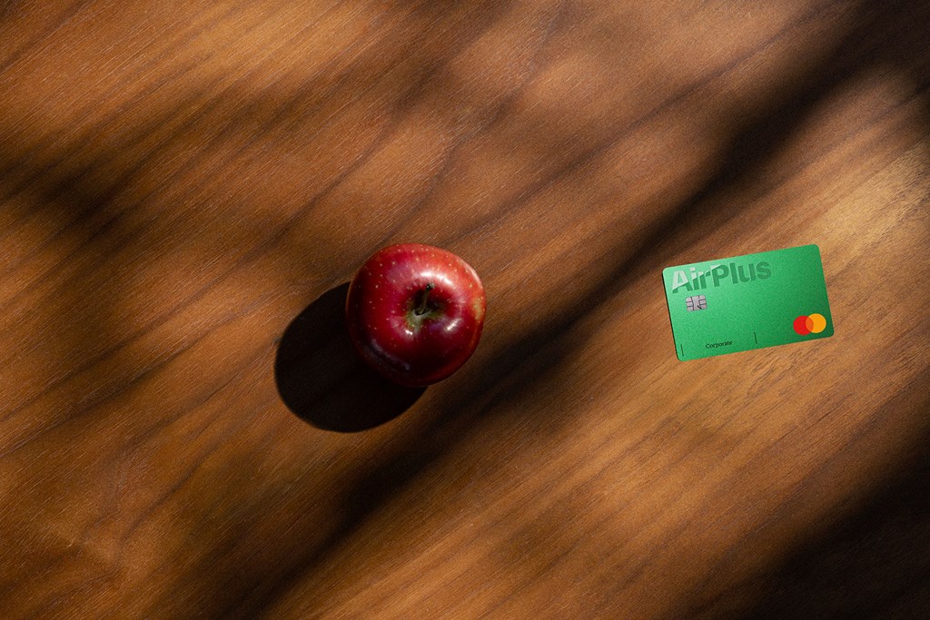 A red apple and a green AirPlus Corporate Card lie on a wooden table in soft light.