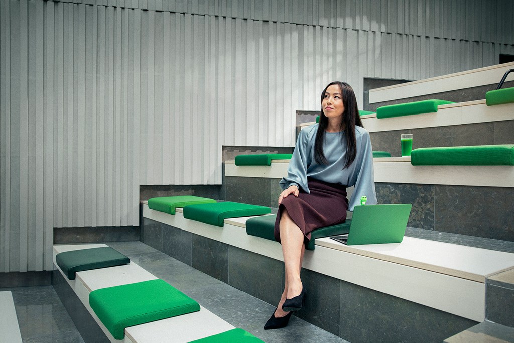 Profesjonell kvinne sitter i et moderne rom med grønne detaljer, med bærbar PC og drikke ved siden av.