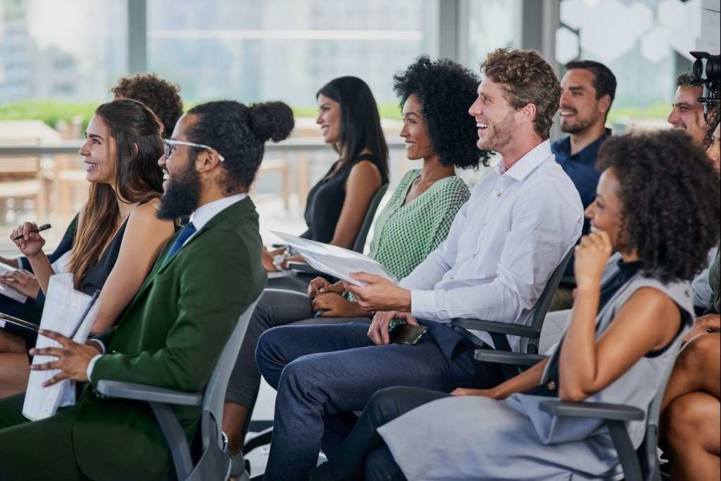 A group of smiling people sit and listen attentively while taking part in an event.