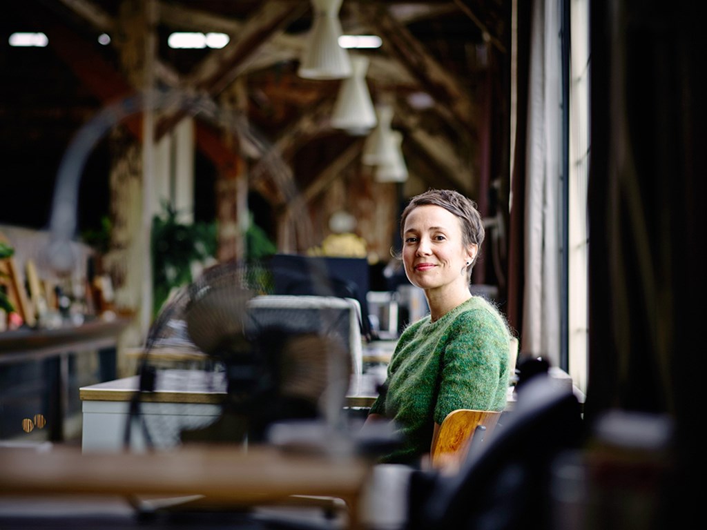 Smiling woman in a green sweater sitting at a desk in an office environment