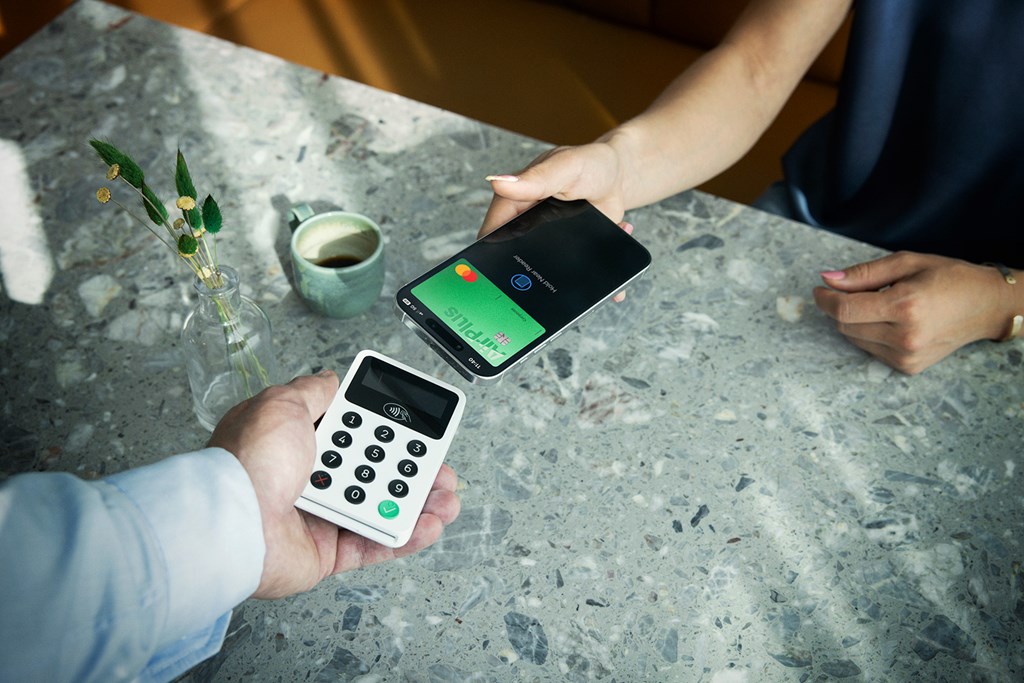 Customer pays with a phone using an AirPlus Corporate Card via contactless terminal on a café table.