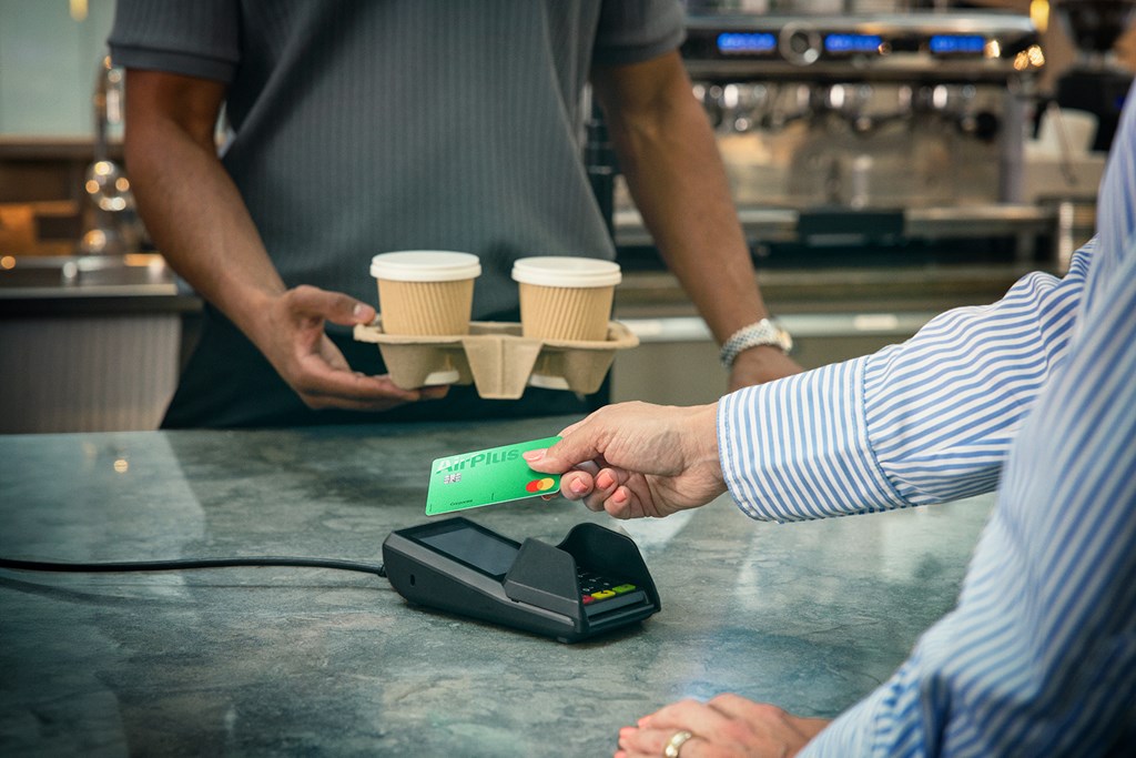 Kunde zahlt kontaktlos mit der AirPlus Firmenkarte, während ein Barista zwei Kaffees hält.
