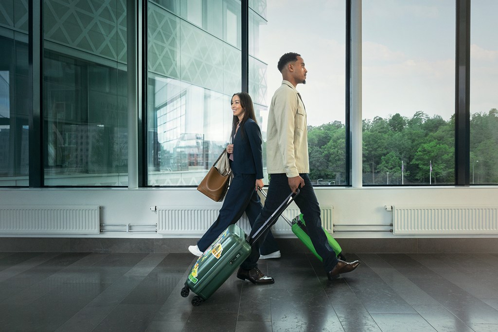 Man and woman walking through an airport corridor with luggage, both dressed in business attire.